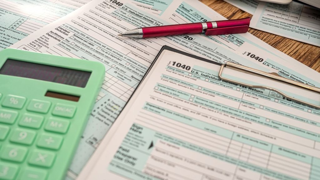 Tax forms 1040 on a tablet with a pen calculator lie on a new wooden table