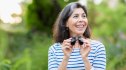 A smiling woman holding binoculars while birdwatching outside to improve her brain health