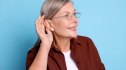 A woman with hearing loss cupping her ear against a blue background