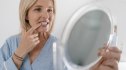 Woman looks in the bathroom mirror, inspecting her gums for symptoms of gingivitis