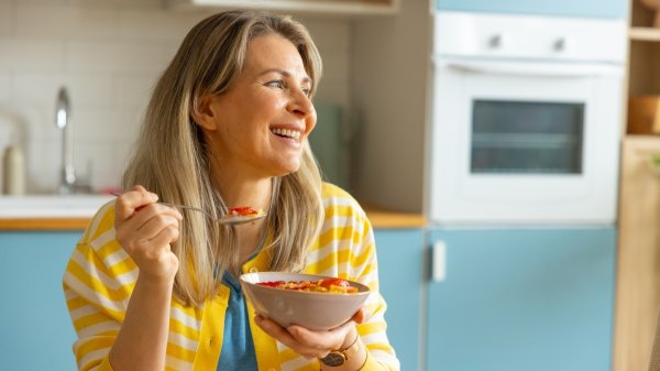 A smiling woman in her kitchen eating healthy foods for weight loss