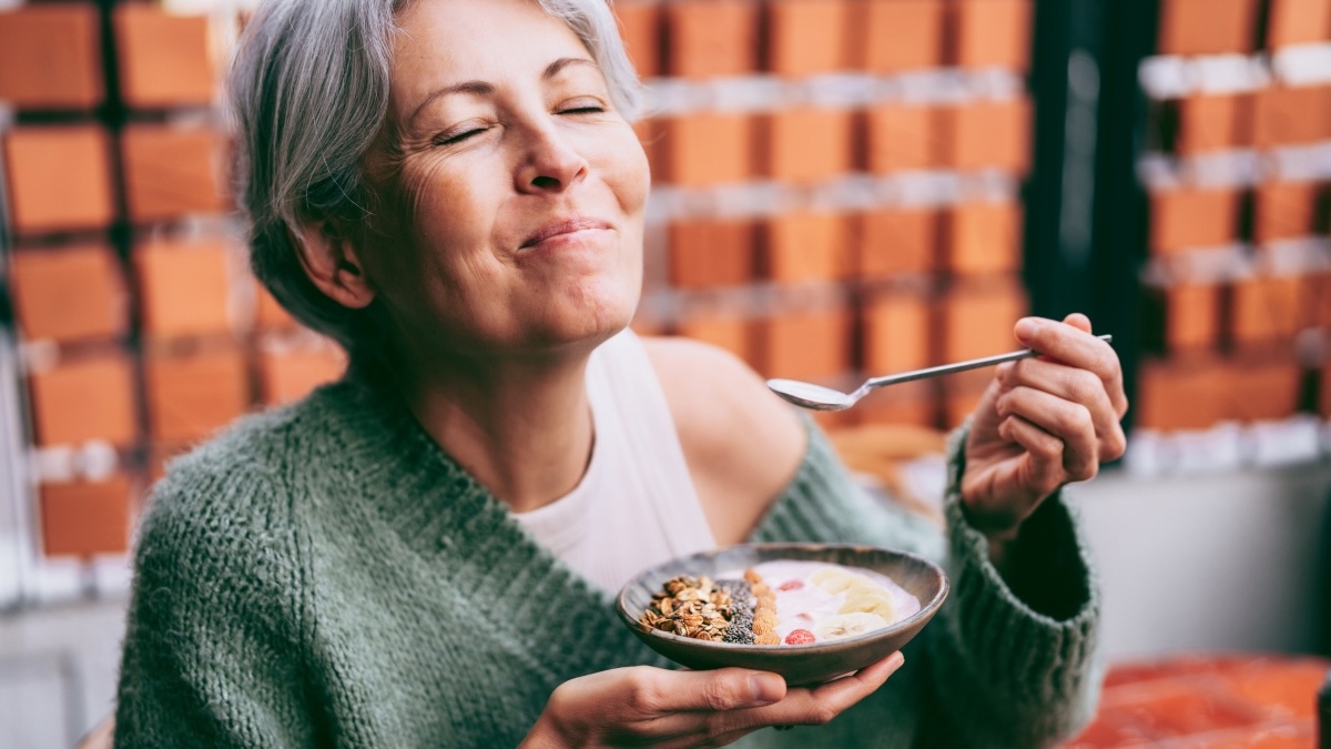A mature woman smiling while eating her healthy hyperfixation meal, a smoothie bowl
