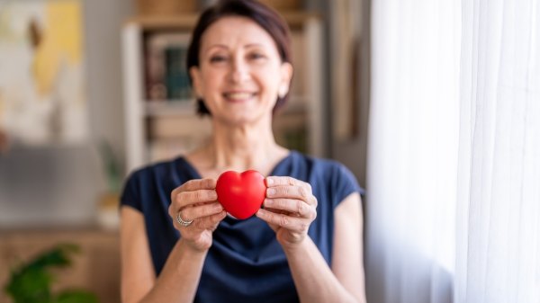 A woman holding a red decorative heart after learning how to lower her cholesterol