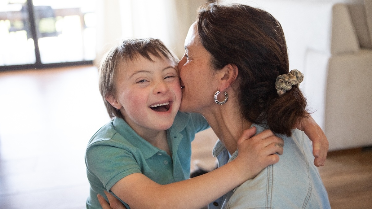 mother embraces her young, smiling son with Down's Syndrome