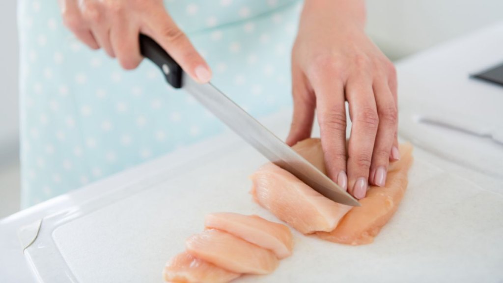 Cropped closeup photo of housewife hands cutting chicken meat