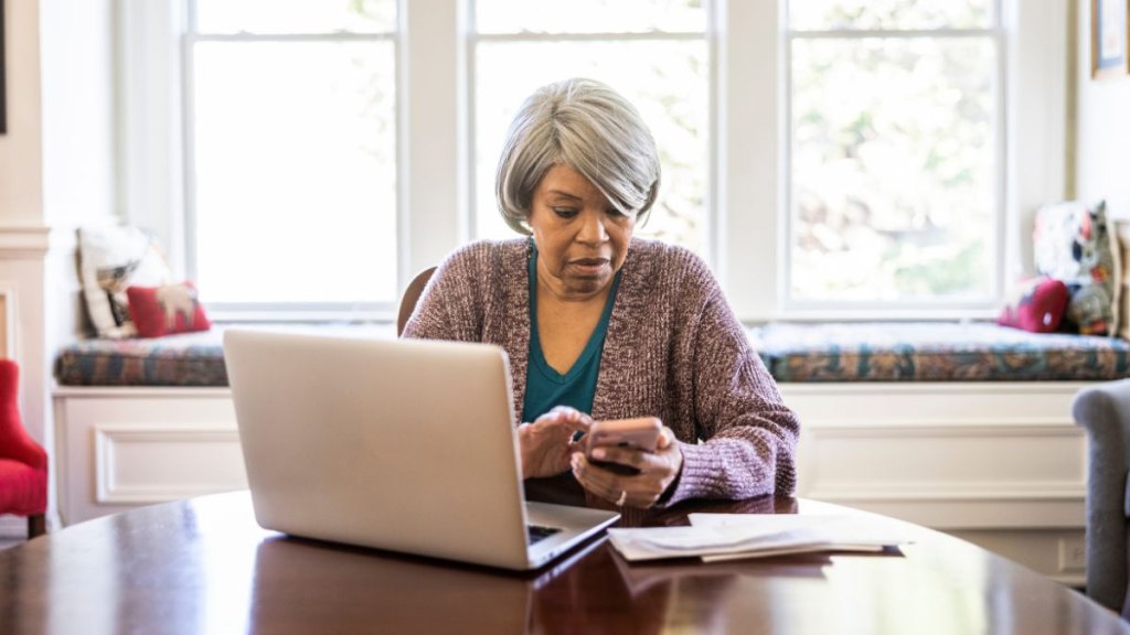 Senior woman paying bills with laptop and smartphone at home