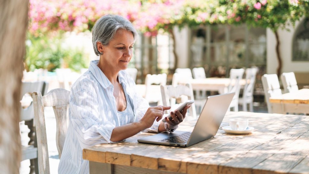 Stylish middle-aged woman with grey hair working on laptop in cozy cafe
