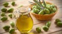 A bottle of extra-virgin olive oil beside a wooden bowl of green olives