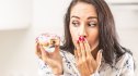 Woman looking guilty after taking a bite of donut due to sugar cravings, which could be a sign of a nutrient deficiency