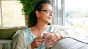 A woman with high blood pressure looking out a window smiling while holding a cup of tea