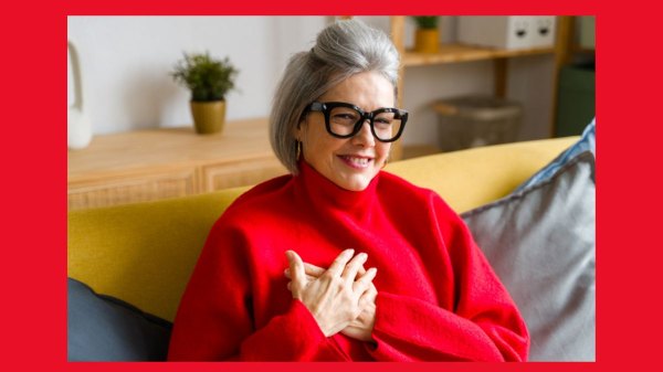 A smiling woman in a pretty red sweater places her hands over her heart to help improve her vagus nerve function