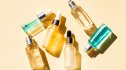 A collection of beauty elixirs and peptides sit in glass bottles against a pale yellow background