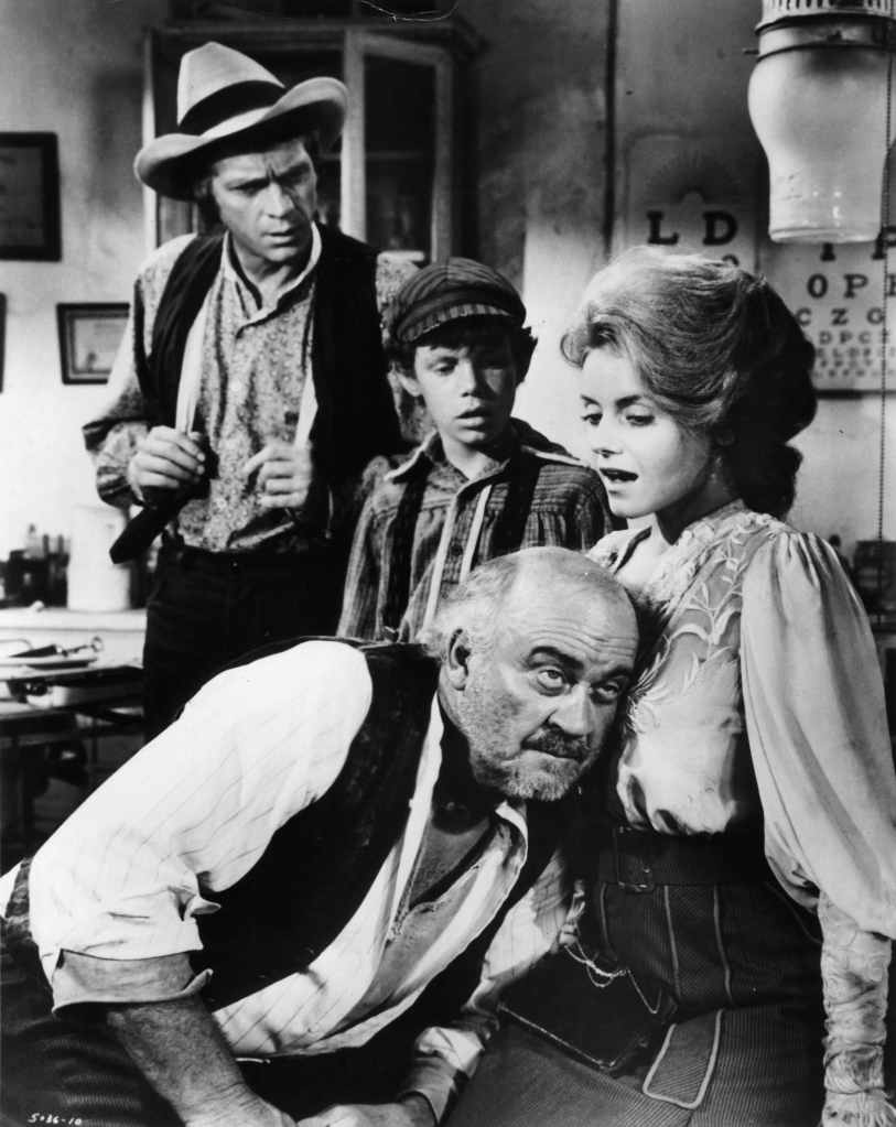 Steve McQueen watches as a man puts his ear against Sharon Farrell's chest in a scene from the film 'The Reivers', 1969.