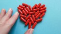 Close-up of a woman's hand touching red statin pills that form a heart shape against a blue background