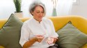 A woman sitting on a couch with pills in her hand, considering if she should stop taking statins