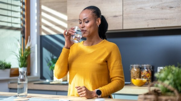 A woman in a yellow shirt taking a berberine pill with a glass of water to help with weight loss