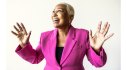 A happy midlife woman proudly wears a bright pink jacket and spreads her arms out to the sides after discovering the benefits of desire