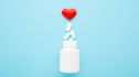 An open bottle of heart medication spilling out against a blue background with a red heart above it