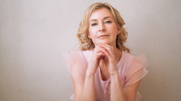 A woman in pink with her hands on her chin thinking about her most recent menopause symptoms