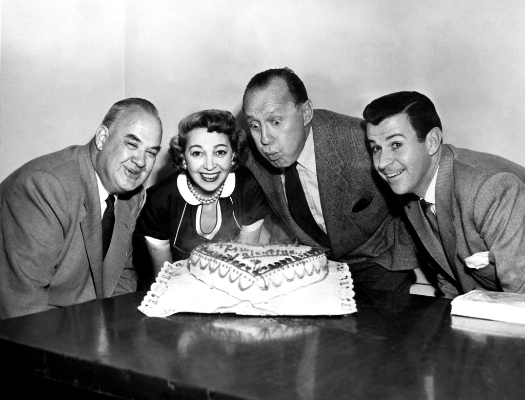 Jack Benny blows out perpetual 39th birthday cake with show announcer Don Wilson, wife Mary Livingstone, Dennis Day, 1954