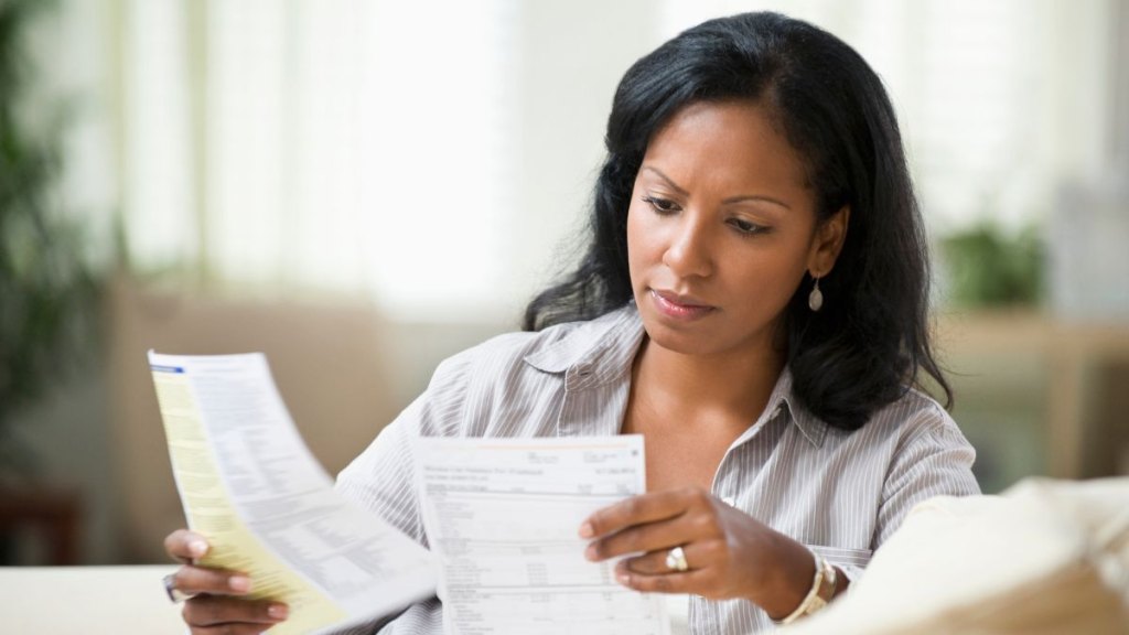 Hispanic woman sitting on sofa reading bills​
