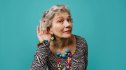 A woman cupping her ear against a teal background, wondering if hearing loss can be reversed
