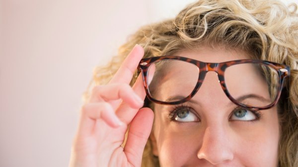 Close-up of a woman with eye floaters lifting her glasses
