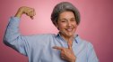 A woman flexing her arm against a pink background after learning how to improve her bone health