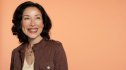 A woman against a peach-colored background smiling after learning how to prevent hair loss