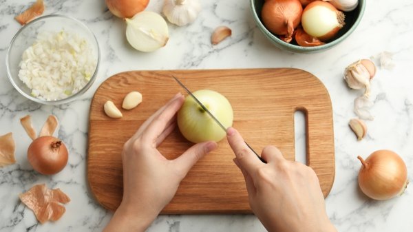 Close-up of a woman's hand cutting onions, which help lower diabetes risk