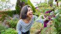 A woman smiling while checking flowers in her garden after learning how to prevent a summer cold