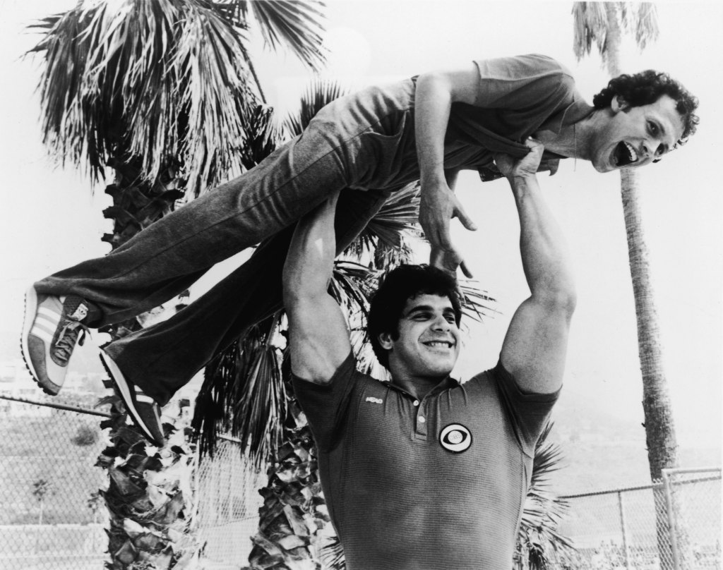 Bodybuilder and actor Lou Ferrigno holds actor and comedian Billy Crystal over his head on the set of the television special, 'Battle of the Network Stars,' c. 1978.
