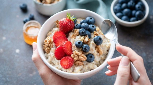 Woman holding a bowl of oats with berries and walnuts, foods that help lower LDL cholesterol