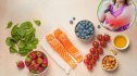A countertop with various anti-inflammatory foods on it such as greens, salmon and blueberries.