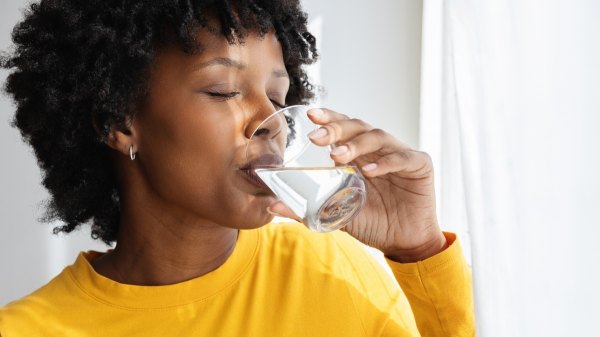 A woman in a yellow top drinking water to get her blood sugar levels down quickly