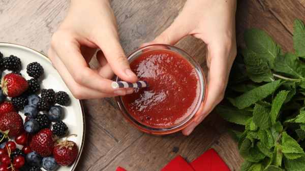 Close-up of a woman's hands holding a smoothie and bowl of berries, both of which help reverse fatty liver disease