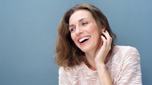 A woman smiling against a blue background after a scalp treatment for hair growth
