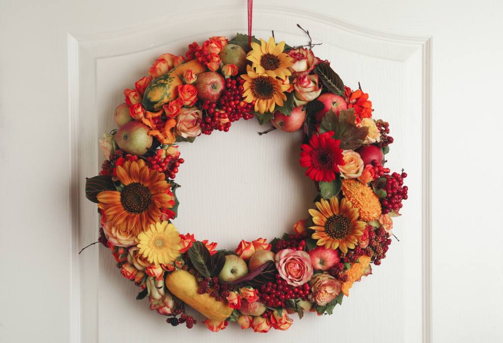 Beautiful autumnal wreath with flowers, berries and fruits hanging on white wooden door.