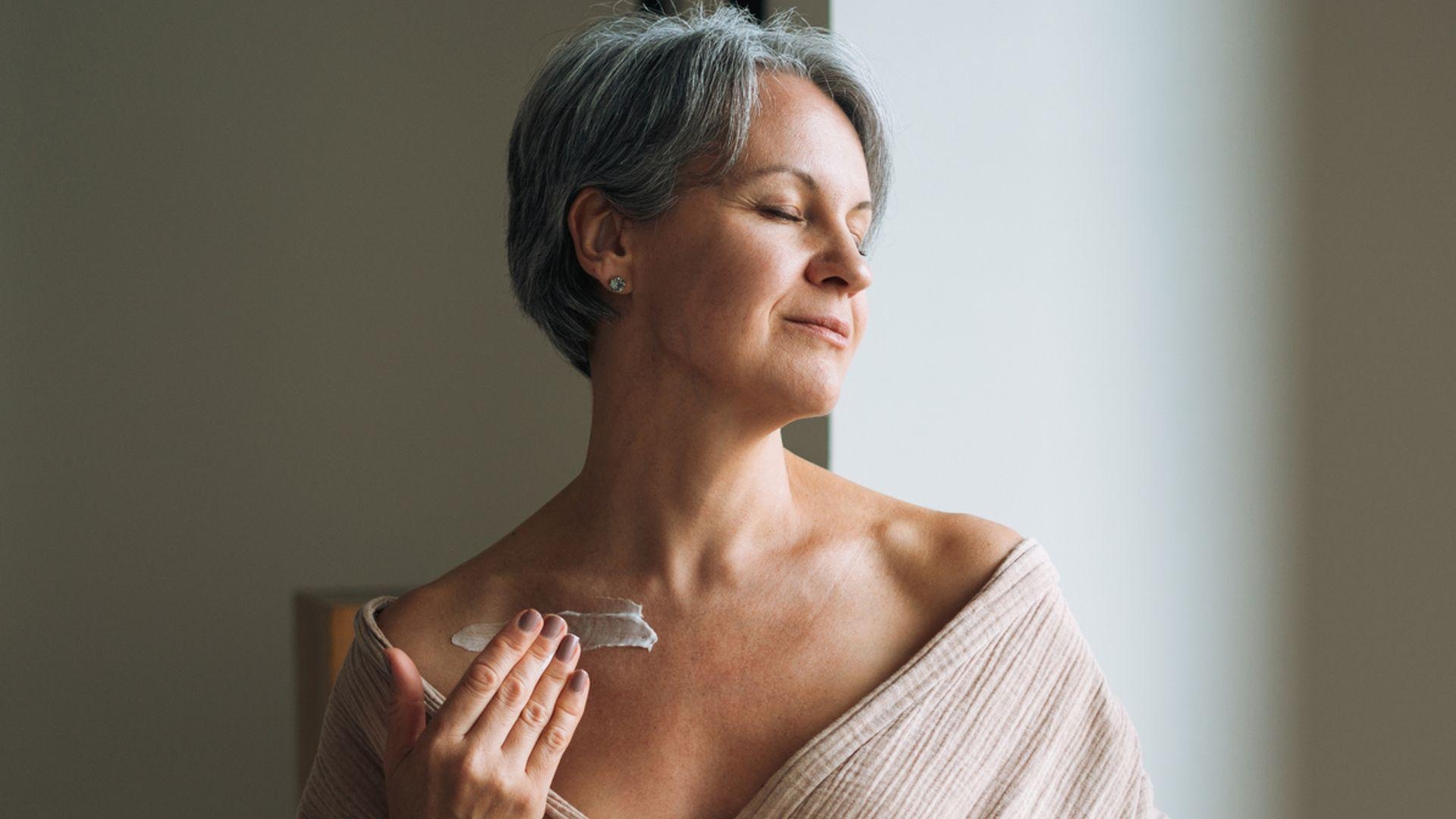 Woman applying neck firming cream to the skin along her jawline and neck