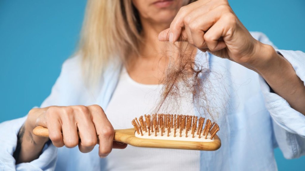 Woman taking her lost hair from brush on light blue background