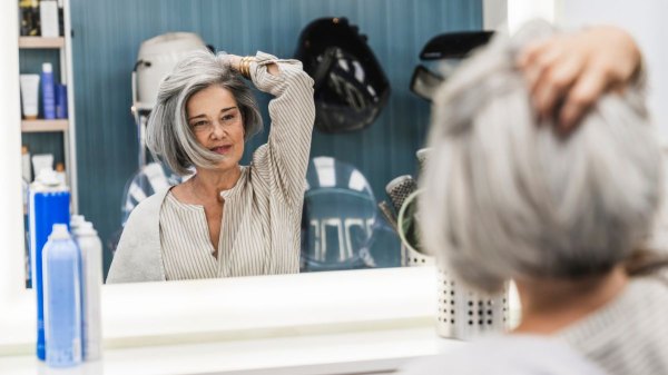 A woman running her hands through her new hair topper while looking in the mirror