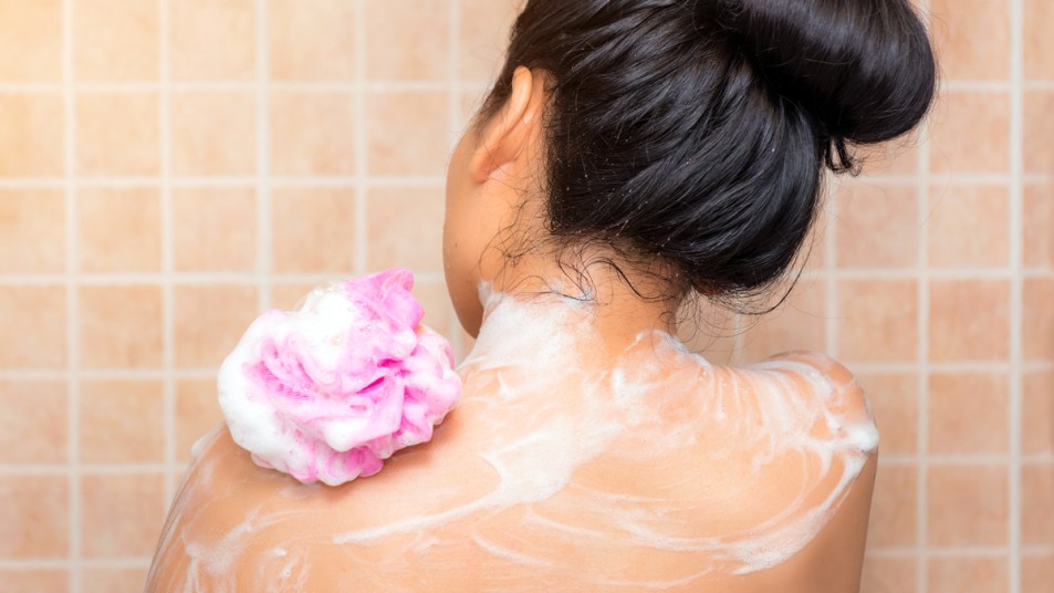 Back of woman using pink loofa in shower