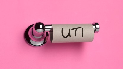 An empty roll of toilet paper with UTI written on it against a pink background