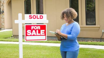 Women stands next to a sold sign holding a checklist that covers What Not to Fix When Selling a House