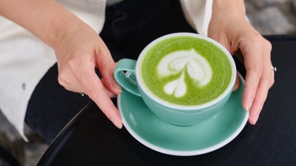 A close-up of a woman holding a cup of matcha, which differs from green tea