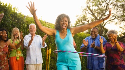 A woman in a blue top and pants hula hooping surrounded by friends to reverse her biological age
