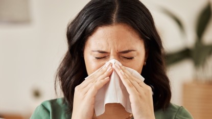 A brunette woman blowing her nose with a tissue because allergies made her stuffy and tired